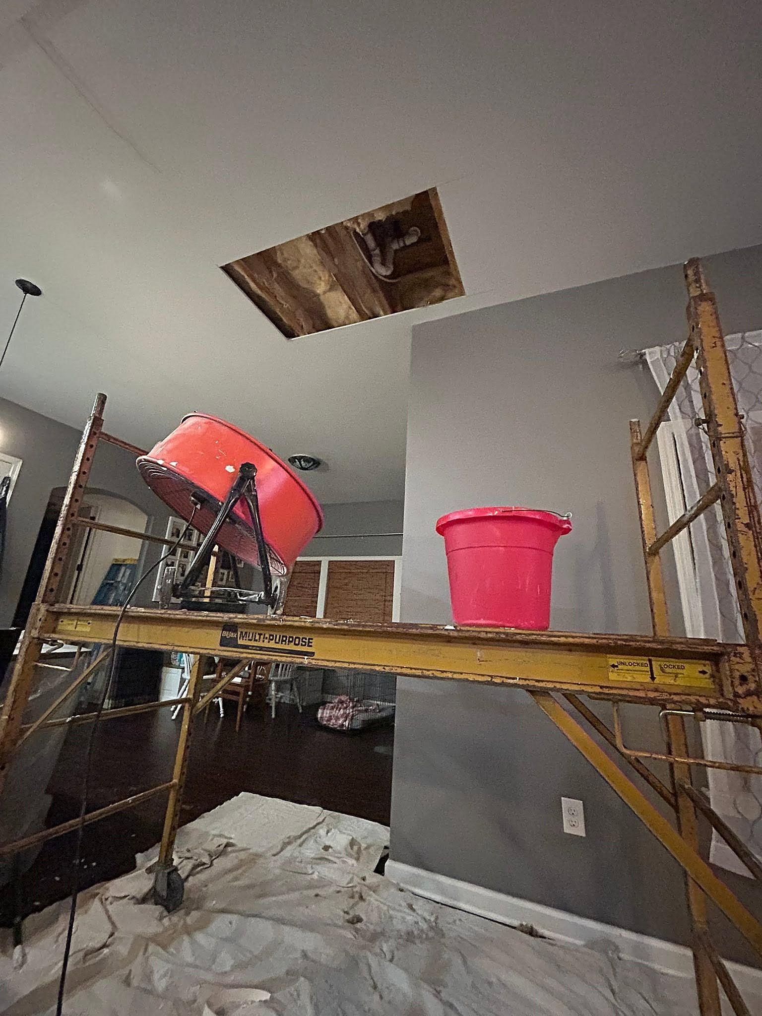 Scaffold holding a fan and bucket below an opened ceiling for drying and water removal