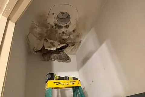 Water-damaged ceiling with dark staining around an air conditioning vent in a closet