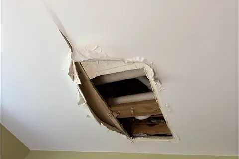 Hole cut in a ceiling exposing PVC drain pipes and wet framing below a bathroom