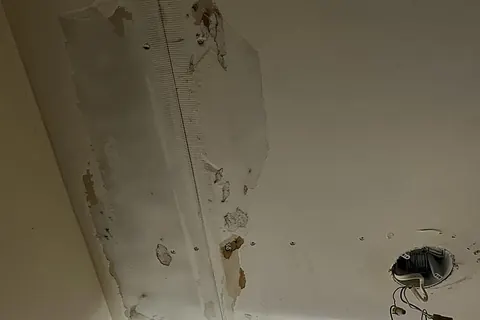 Ceiling drywall peeling away with mesh tape exposed and a light fixture removed