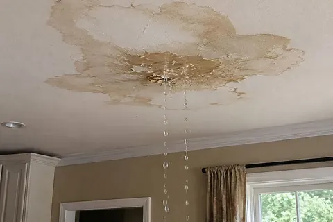 Large brown water stain on a ceiling with water actively dripping into the room