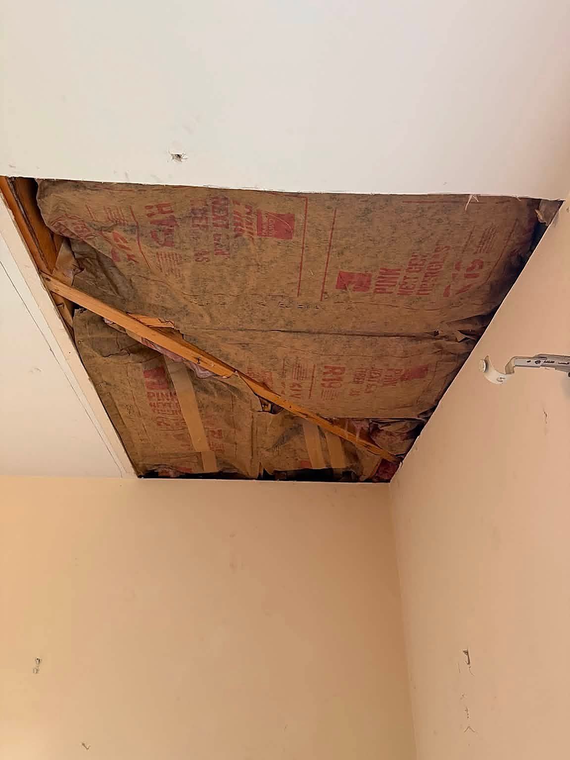 Wet stained fiberglass insulation exposed through an opened ceiling after a roof leak